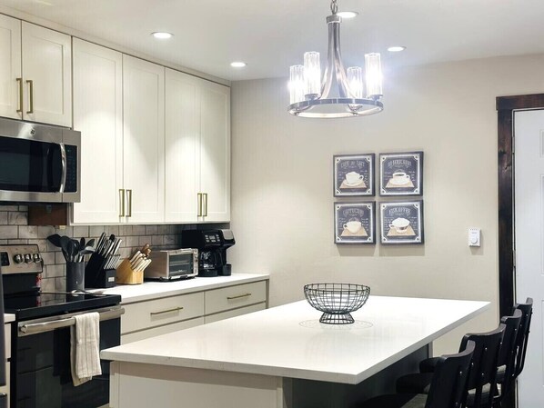 A modern kitchen with a central island, stainless steel appliances, and a chandelier.