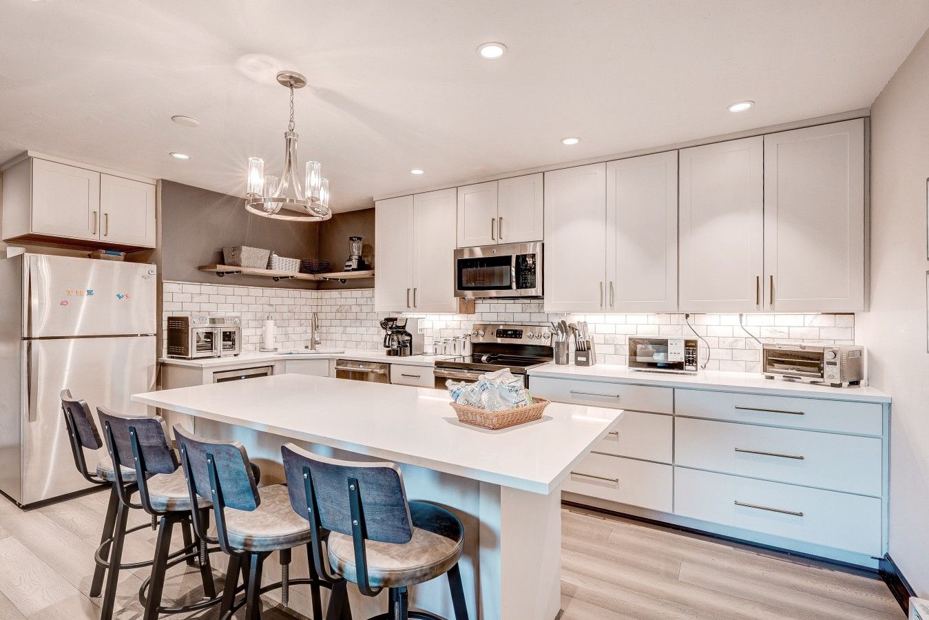 Une cuisine moderne avec des meubles blancs, un îlot central doté de tabourets et des appareils électroménagers intégrés.