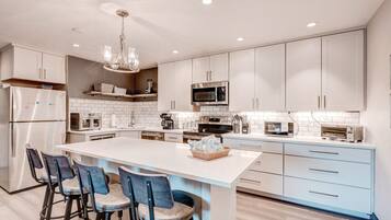 Une cuisine moderne avec des meubles blancs, un îlot central doté de tabourets et des appareils électroménagers intégrés.