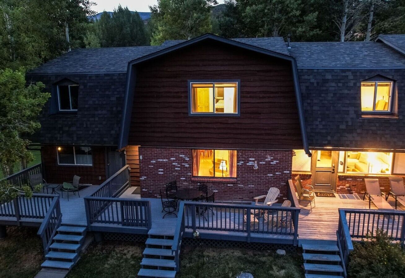 Une maison à deux étages dotée d’une terrasse, d’un escalier et d’un espace patio am énagé avec du mobilier d’extérieur.