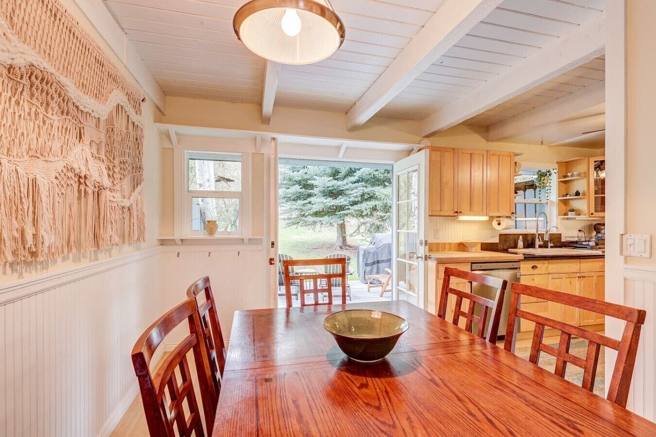 Un coin repas avec une table et des chaises en bois, une décoration murale et une vue sur l’extérieur par une porte.