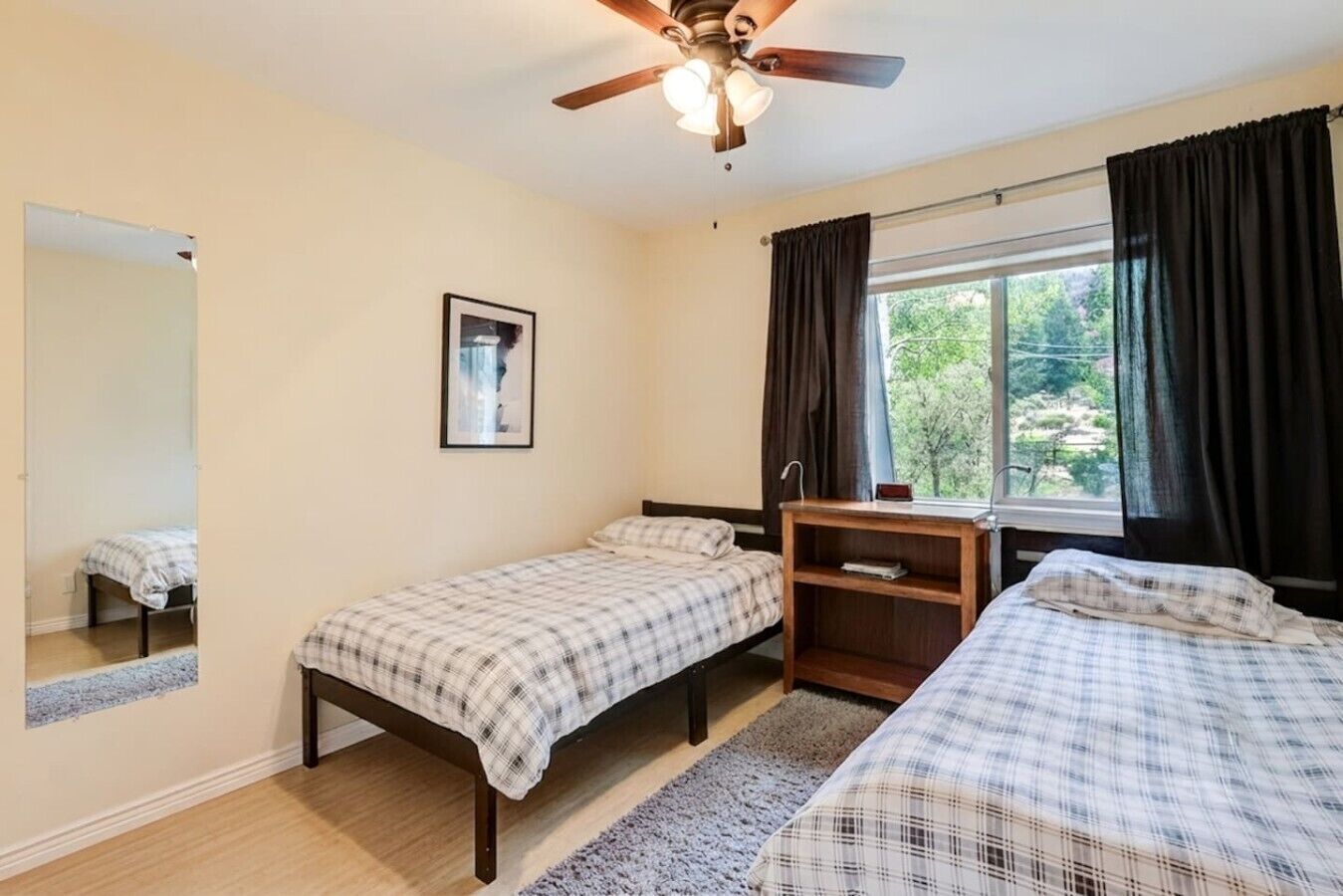 A room with two beds, a ceiling fan, a window with curtains, and a framed picture on the wall.