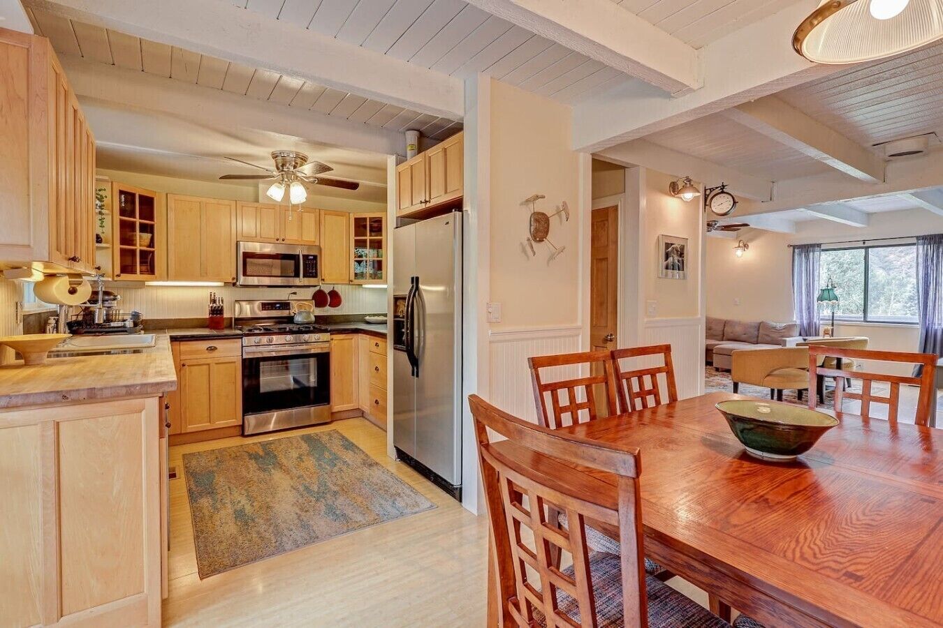 Una cocina moderna con armarios de madera, un refrigerador de acero inoxidable y un comedor con mesa y sillas de madera.