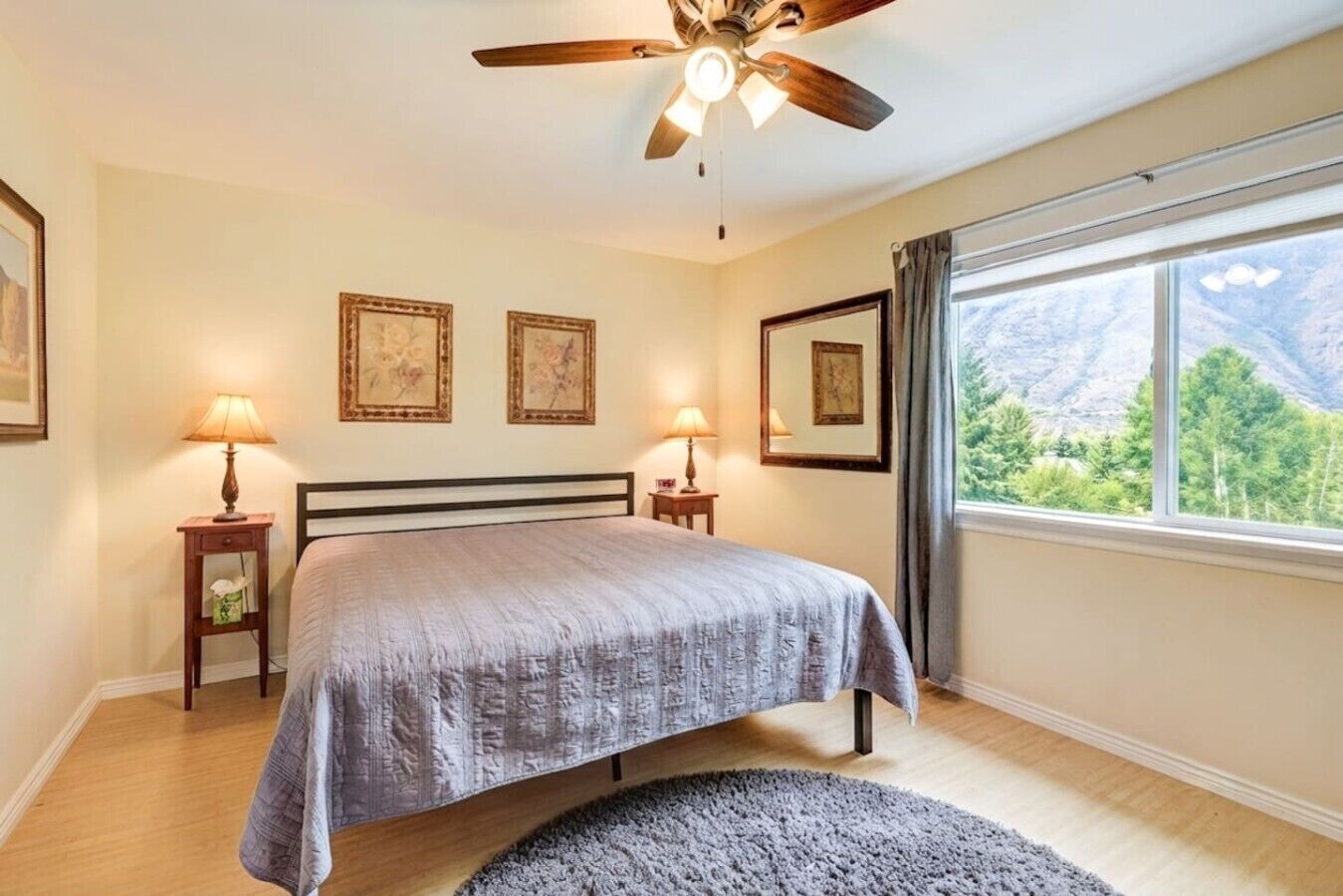 Une chambre à coucher comprenant un lit, deux tables de chevet, un ventilateur de plafond et une fenêtre donnant sur la montagne.