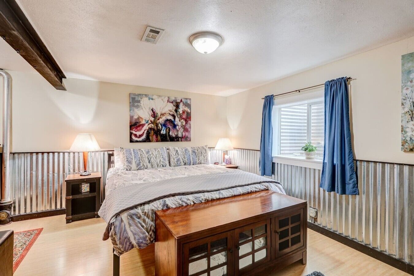 Ein Schlafzimmer mit Bett, Nachttischlampen, einem Fenster mit Vorhängen, einer Heizung und einem Bild an der Wand.