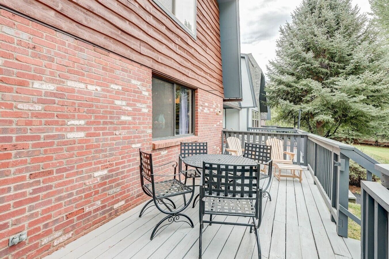 Une terrasse en bois avec des meubles d’extérieur, un mur en briques et une vue sur un arbre.