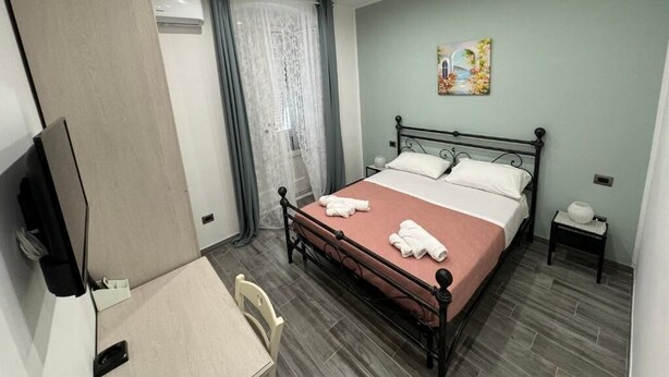 A hotel room with a bed, a desk, a chair, a TV, and a painting on the wall.