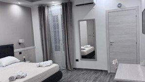 A hotel room with a bed, a desk, a mirror, and an air conditioning unit.