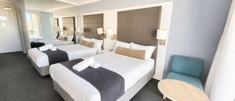 Habitación de hotel con dos camas, una mesita redonda y una silla azul.