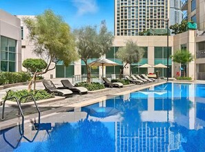 A swimming pool with lounge chairs and umbrellas, surrounded by buildings and trees. - Burj Views Studio - Downtown Dubai -Bills Included (Dubai)