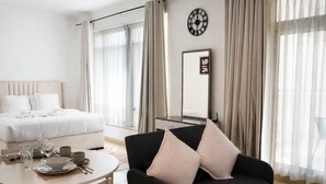 A hotel room with a bed, a dining table with chairs, a black sofa with cushions, a clock on the wall, and sheer curtains. - Burj Views Studio - Downtown Dubai -Bills Included (Dubai)