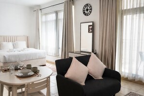 A hotel room with a bed, a dining table with chairs, a black sofa with cushions, a clock on the wall, and sheer curtains. - Burj Views Studio - Downtown Dubai -Bills Included (Dubai)