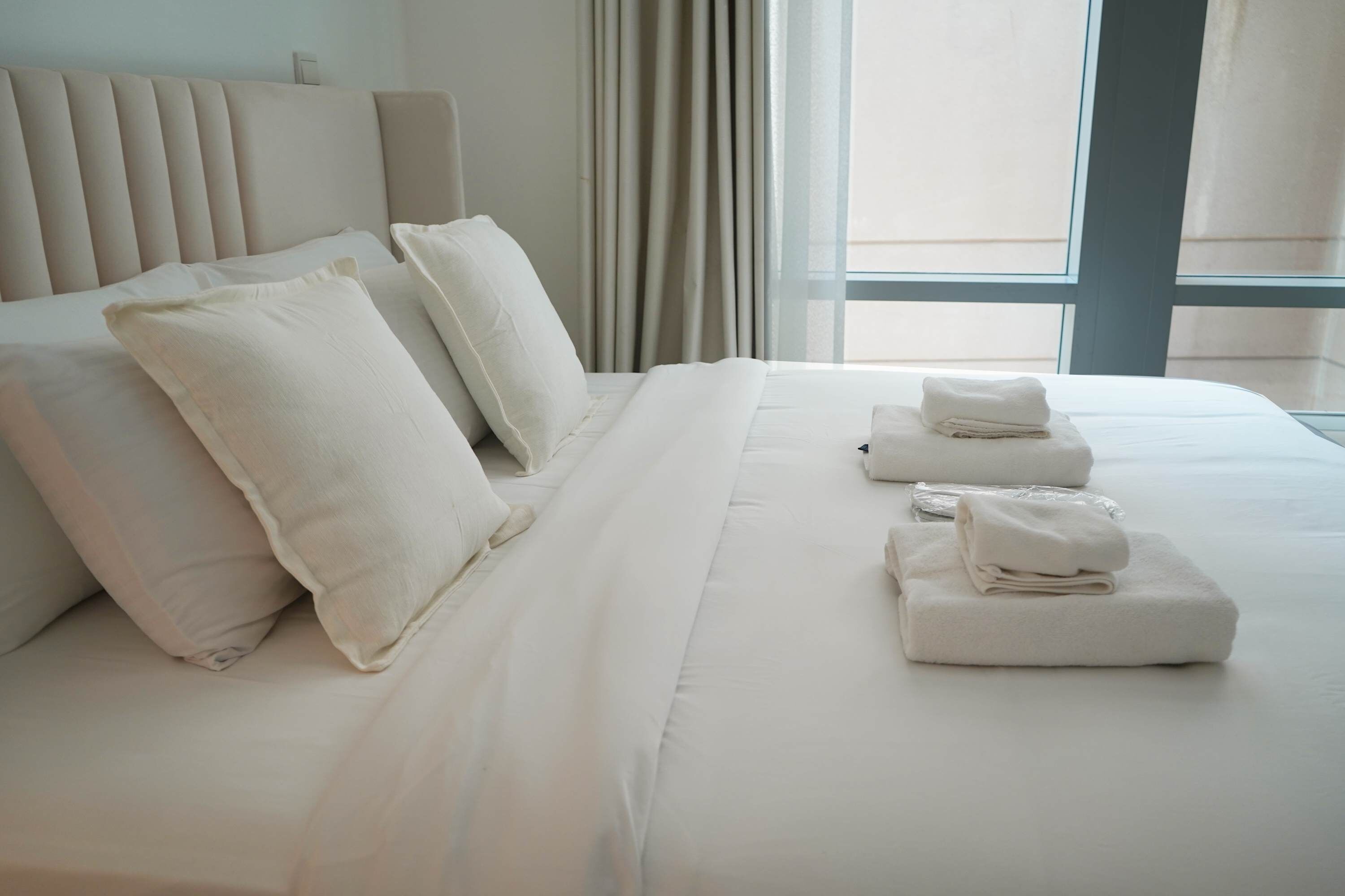 Een hotelkamer met een groot bed, meerdere kussens en netjes gevouwen handdoeken op het bed.