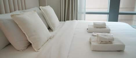 A hotel room with a large bed, multiple pillows, and neatly folded towels on the bed.