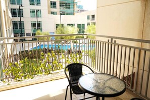 Un balcó amb taula i cadira de vidre, amb vista a una piscina i edificis.