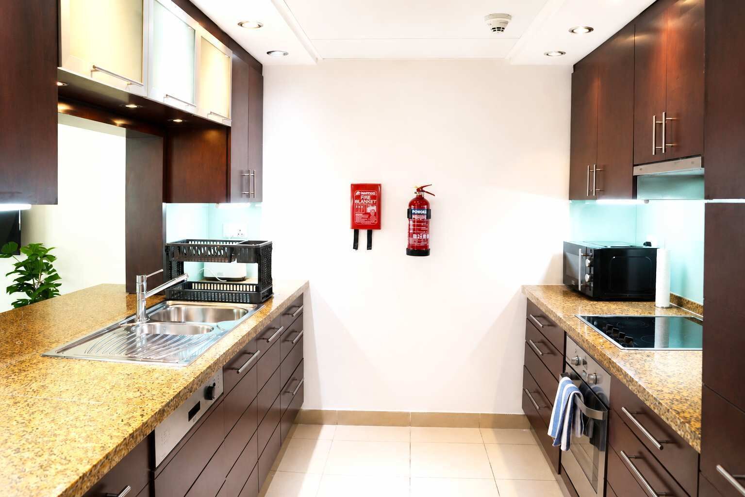 Een moderne keuken met granieten aanrechtbladen, roestvrijstalen apparatuur en donkere houten keukenkastjes.