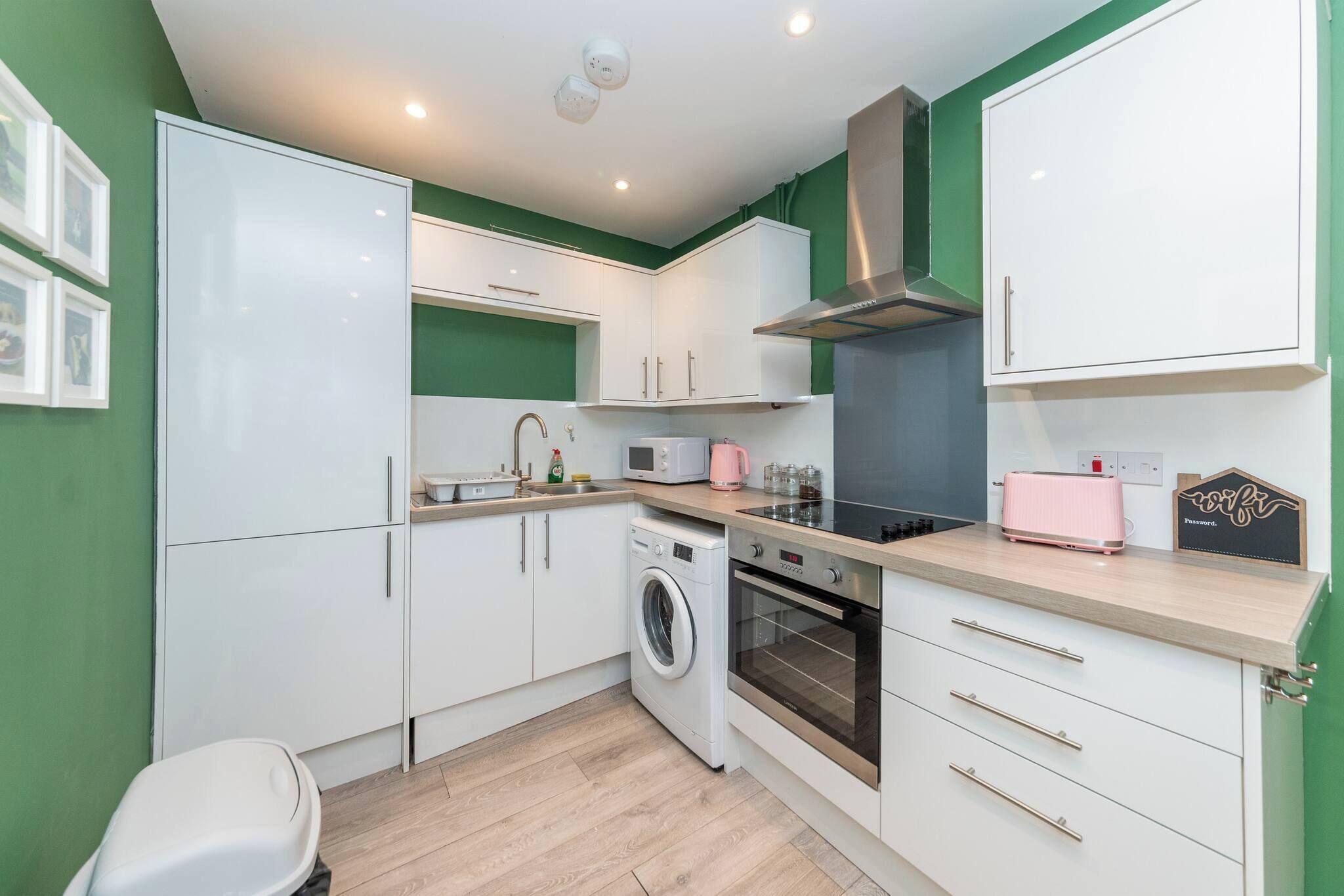 A compact kitchen with white cabinets, a washing machine, an oven, and a microwave.