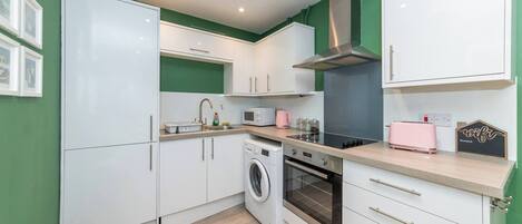 A compact kitchen with white cabinets, a washing machine, an oven, and a microwave.