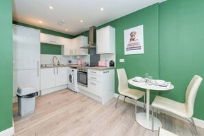 Een compacte keuken met witte kasten, een wasmachine en een eethoek met een witte tafel en stoelen.