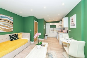 A modern apartment with a green wall, a sofa, a dining table, and a kitchen area. - IBEX HOUSE Free parking 2Bed Fully equipped Flat (Reading)