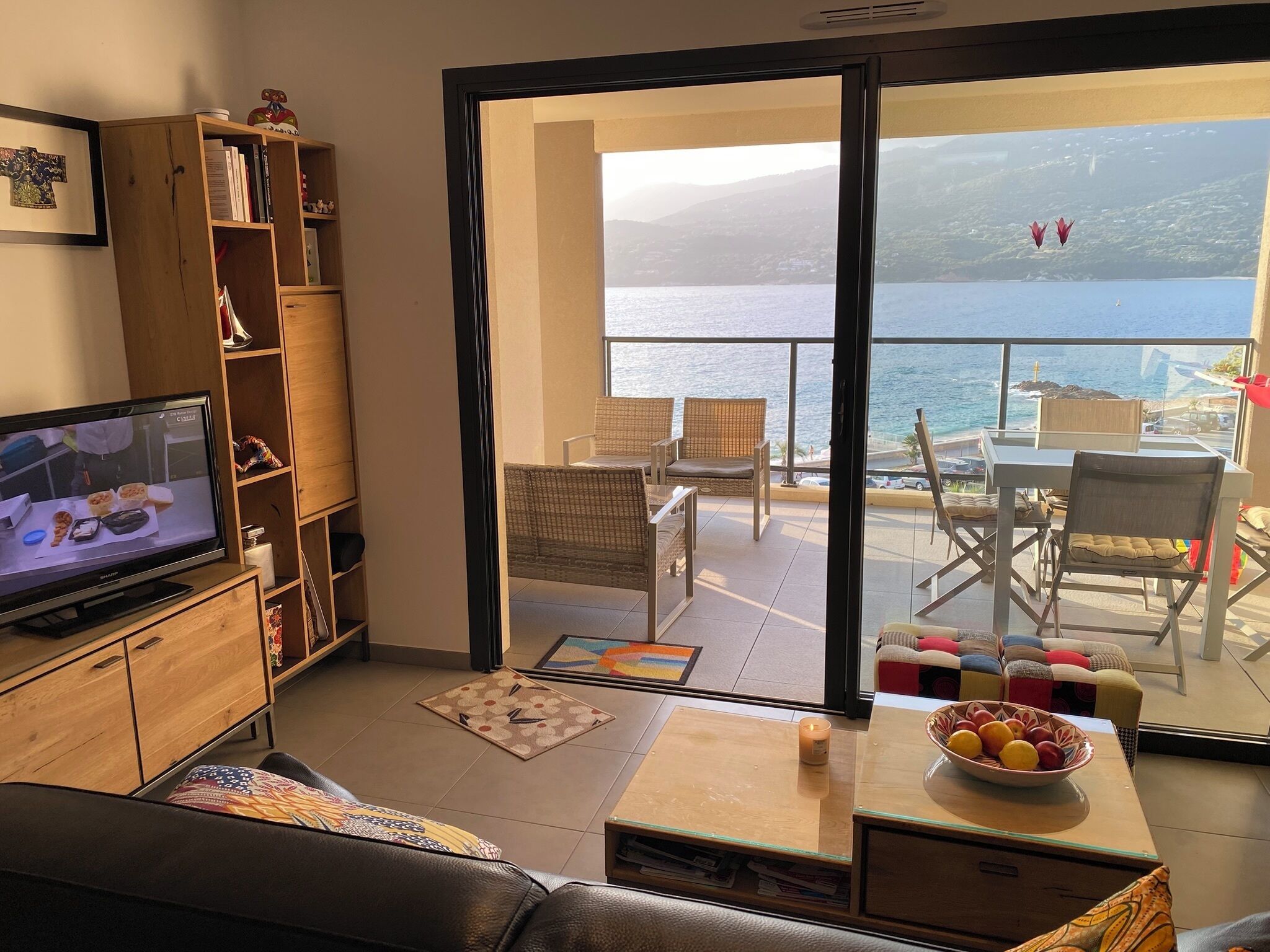Un salon équipé d’un téléviseur, d’une bibliothèque, d’un canapé et offrant une vue sur la mer grâce à une porte vitrée.
