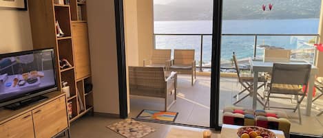 Un salon équipé d’un téléviseur, d’une bibliothèque, d’un canapé et offrant une vue sur la mer grâce à une porte vitrée.