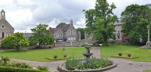 A historic building with a church tower, a fountain, and well-maintained gardens.