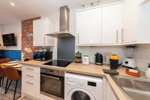 Una cocina moderna con armarios blancos, extractor de acero inoxidable, microondas, tostadora, cafetera y lavavajillas.