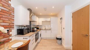 A compact kitchen with white cabinets, a microwave, a stove, and a washing machine. - IBEX HOUSE Cozy Modern 2-Bed Flat • Free Parking (Reading)