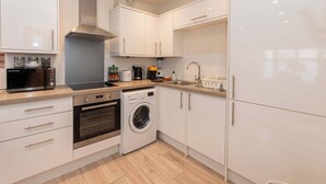 A modern kitchen with a built-in oven, microwave, and washing machine, along with a sink and cabinets. - IBEX HOUSE Cozy Modern 2-Bed Flat • Free Parking (Reading)