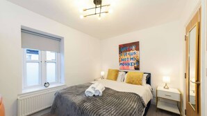 A bedroom with a bed, bedside tables, a window, a radiator, and a painting on the wall. - IBEX HOUSE Cozy Modern 2-Bed Flat • Free Parking (Reading)