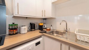 A modern kitchen with white cabinets, a stainless steel sink, a coffee maker, and a dishwasher. - IBEX HOUSE Cozy Modern 2-Bed Flat • Free Parking (Reading)