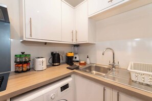 Eine moderne Küche mit weißen Schränken, einer Edelstahl-Spüle, einer Kaffeemaschine und einem Geschirrspüler.