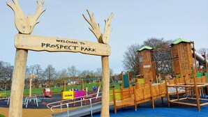 A wooden sign welcoming visitors to Prospect Park with playground equipment in the background.