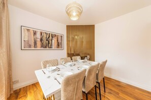 Ein Essbereich mit einem weißen Tisch, gedeckt für sechs Personen, einschließlich Teller, Gläsern und Besteck. An der Wand hängt ein gerahmtes abstraktes Gemälde und es gibt eine vertikale Holzvertäfelung.