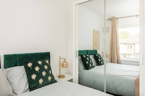 Een hotelkamer met een bed, nachtkastje, lamp en een grote spiegel die de kamer weerspiegelt.