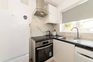 Eine kompakte Küche mit weißen Schränken, einer Edelstahl-Spüle, einem Wasserkocher aus Glas und einem eingebauten Backofen.