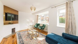 Un salon avec un canapé bleu, un tapis à motifs, un téléviseur fixé au mur et une fenêtre avec des rideaux.