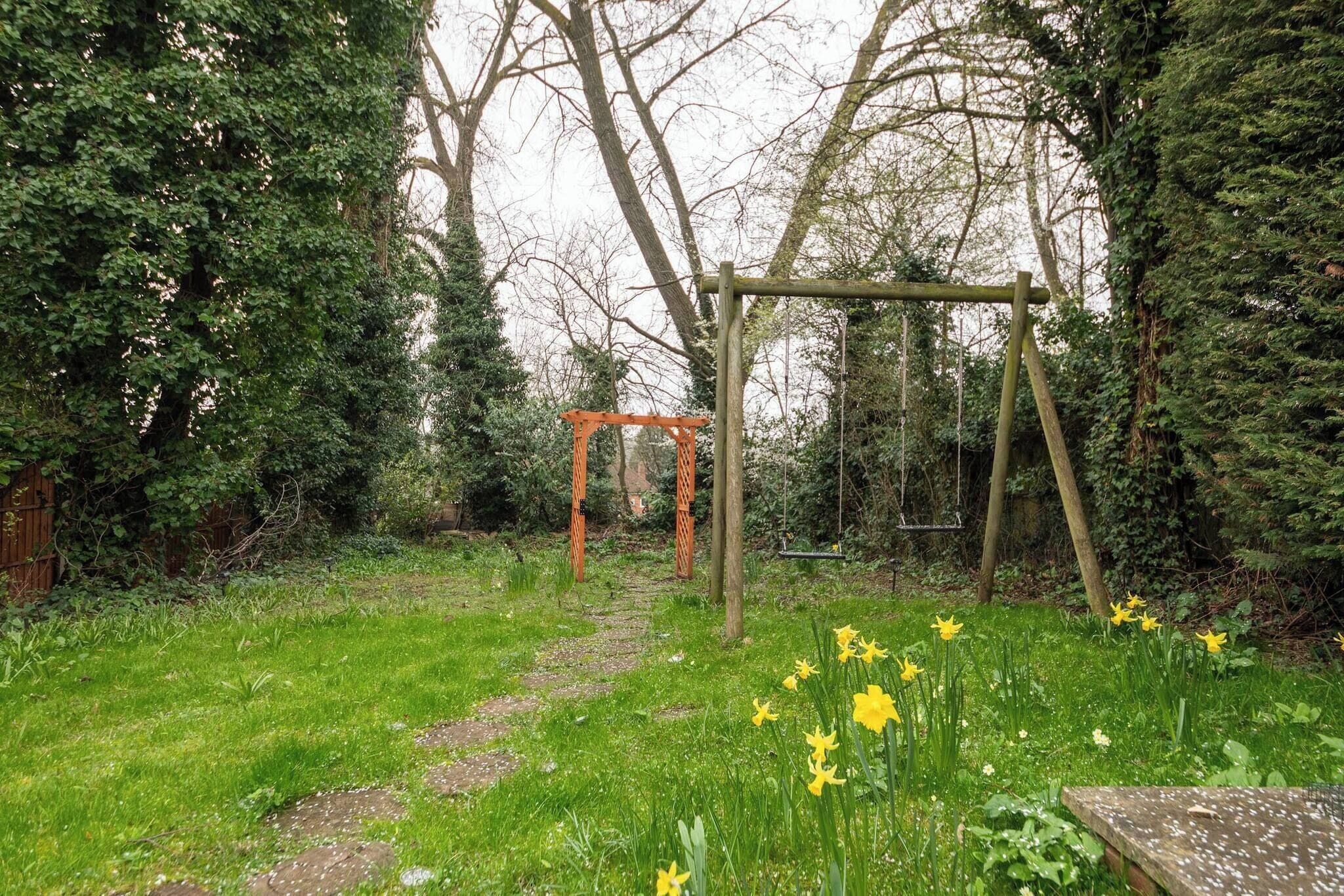 Un jardin avec une balançoire en bois, un sentier et des jonquilles jaunes.