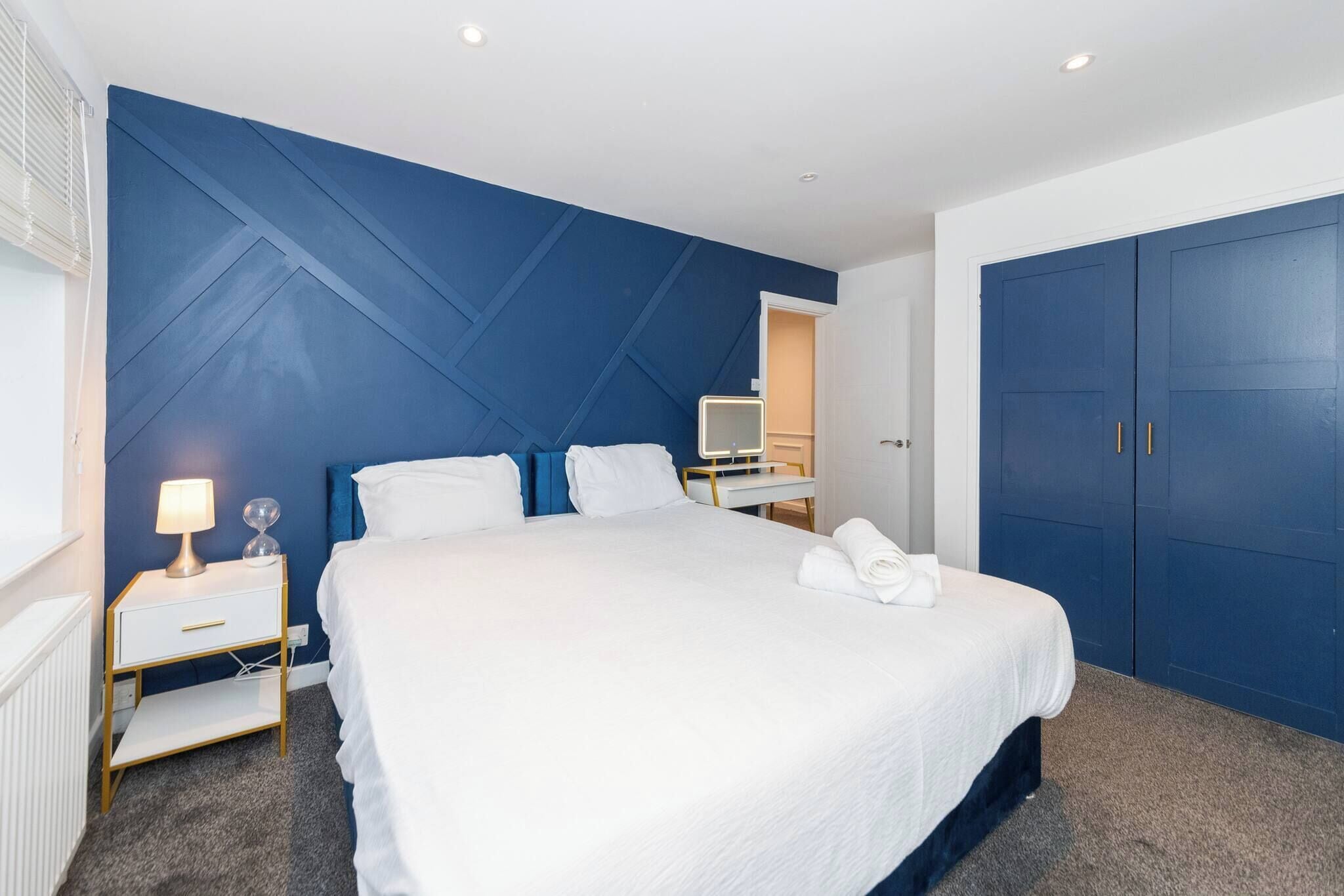 Habitación de hotel con una cama grande, una mesita de noche con lámpara, un espejo y un armario.