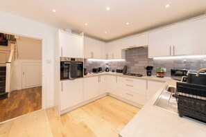A modern kitchen with white cabinets, a built-in oven, a gas stove, and a stainless steel sink. - Spacious 4BR Home with Games Room & Free Parking (Berkshire)