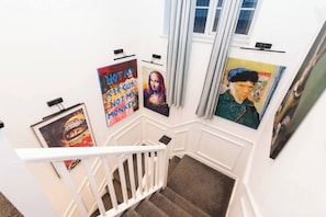 A staircase with white railings and a carpeted floor, leading to a landing with artwork on the walls. - Spacious 4BR Home with Games Room & Free Parking (Berkshire)