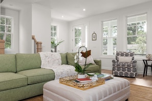 Een woonkamer met een groene bank, een fauteuil met een patroon en een salontafel met boeken en een plant.