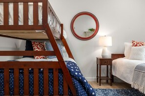 Ein Schlafzimmer mit Etagenbett, Nachttisch mit Lampe, rundem Spiegel und Bett mit Kissen und Decke.