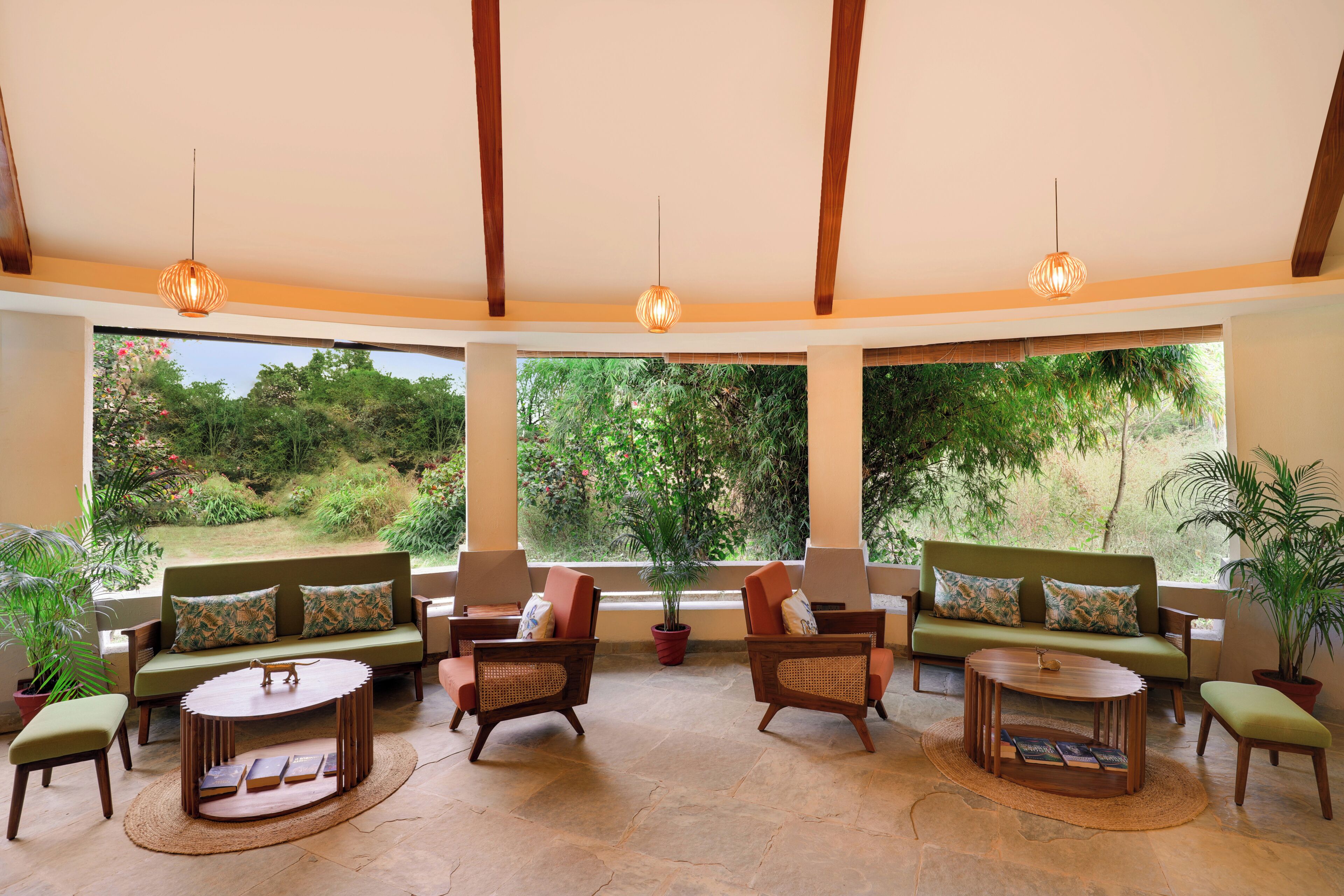 A spacious room with a high ceiling, wooden beams, and large windows offering a view of a lush garden.