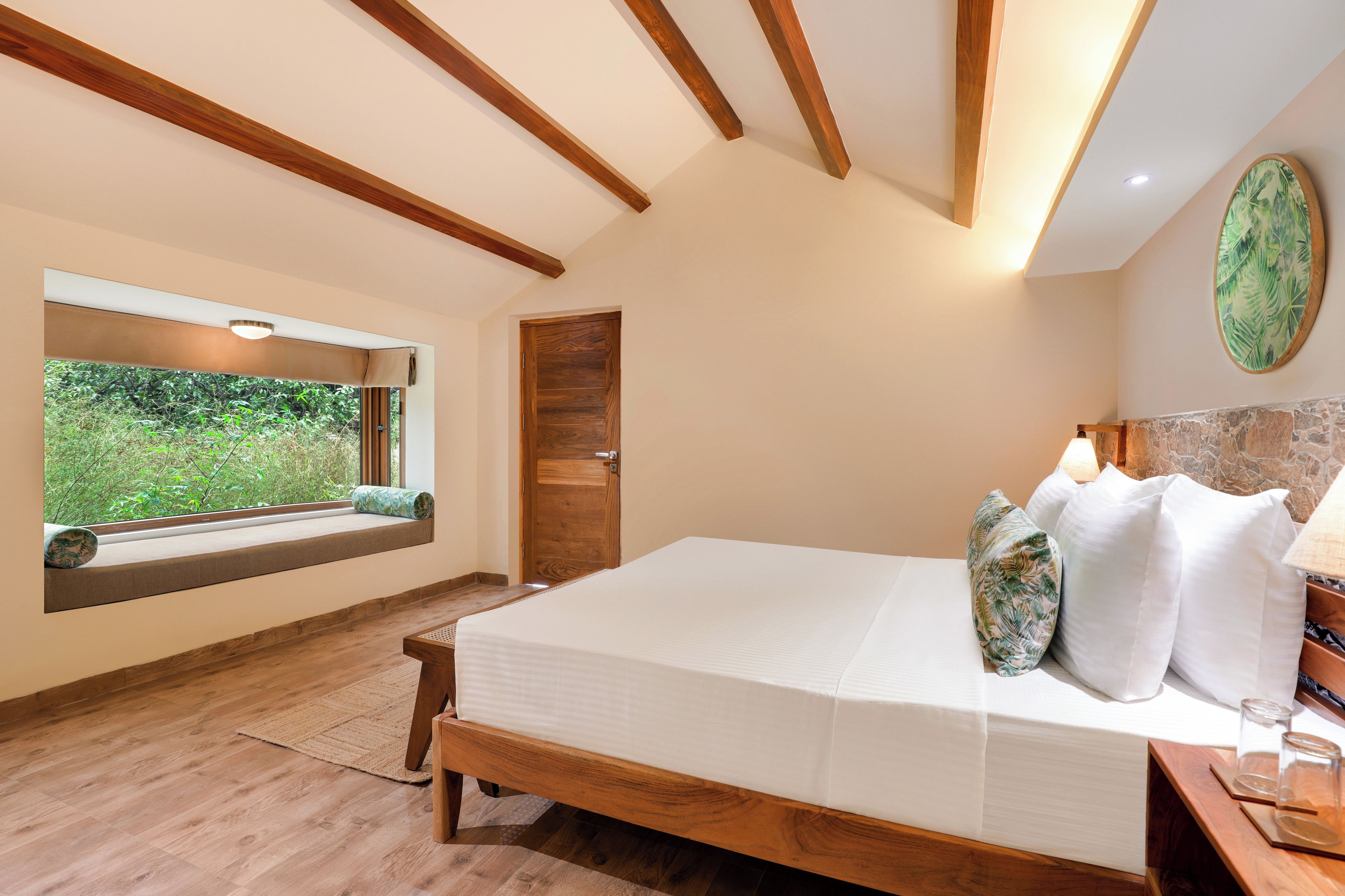 Un dormitorio con cama de madera, ventana con vista a follaje y pared de piedra decorativa.