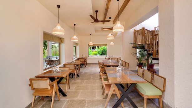 Un vaste espace dédié à la salle à manger, avec des tables et des chaises en bois, de grandes fenêtres et des luminaires suspendus.