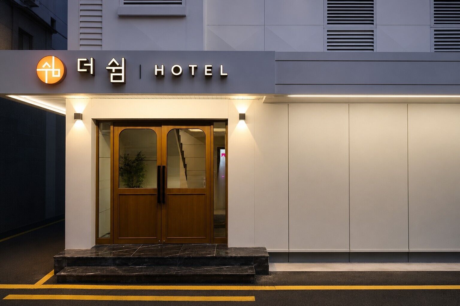 Entrada de hotel con un letrero, puertas dobles y una escalera que lleva a la entrada.