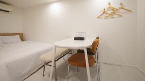 A hotel room with a bed, a small table, a chair, and a wall-mounted hanger.