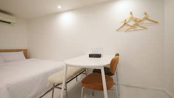 A hotel room with a bed, a small table, a chair, and a wall-mounted hanger.